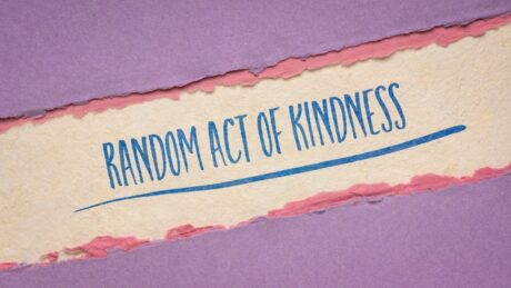 Random act of kindness written on torn paper with purple and pink background.