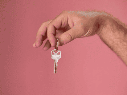 Key held by hand on pink background, symbolizing homeownership and real estate in Tampa.