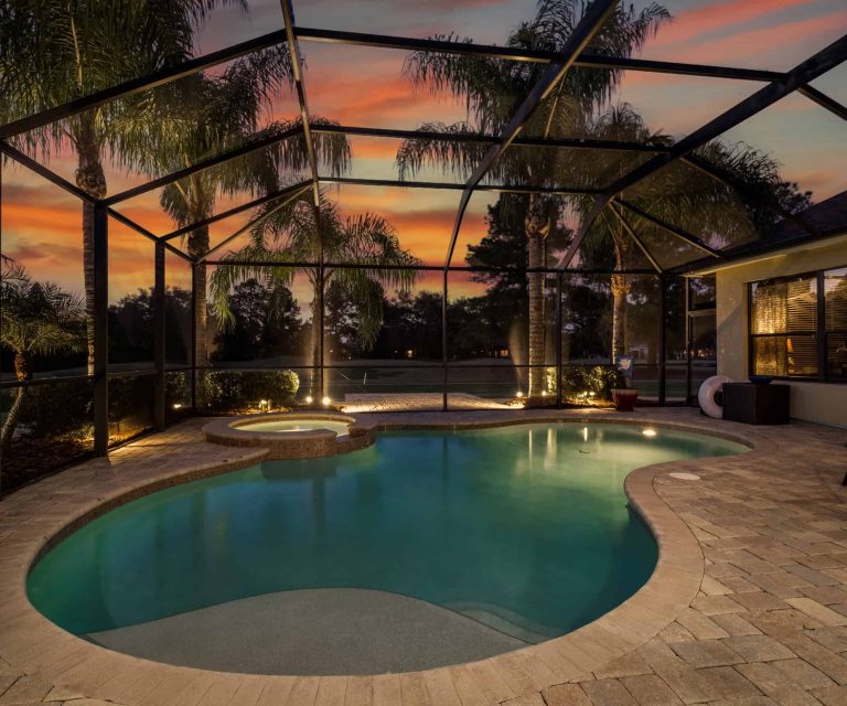 Spacious screened-in pool enclosure with a heated pool and hot tub at sunset.